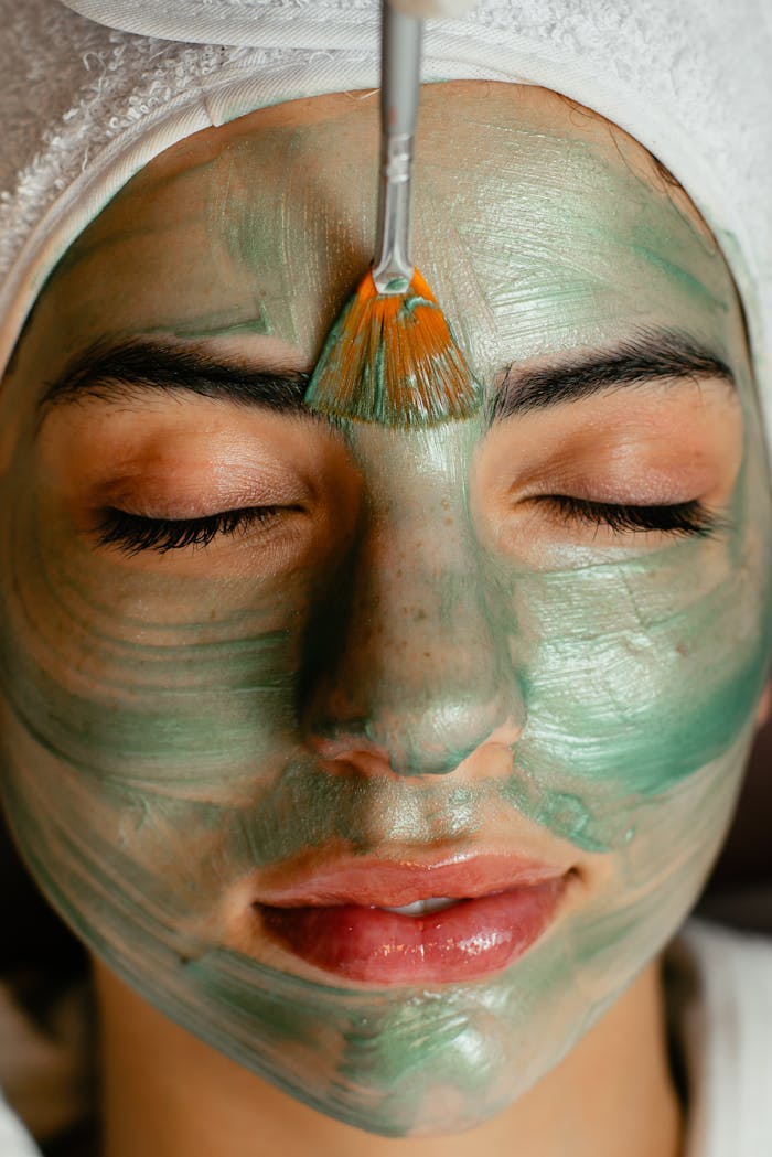 Close-up of a woman enjoying a green cosmetic facial mask application at a spa.